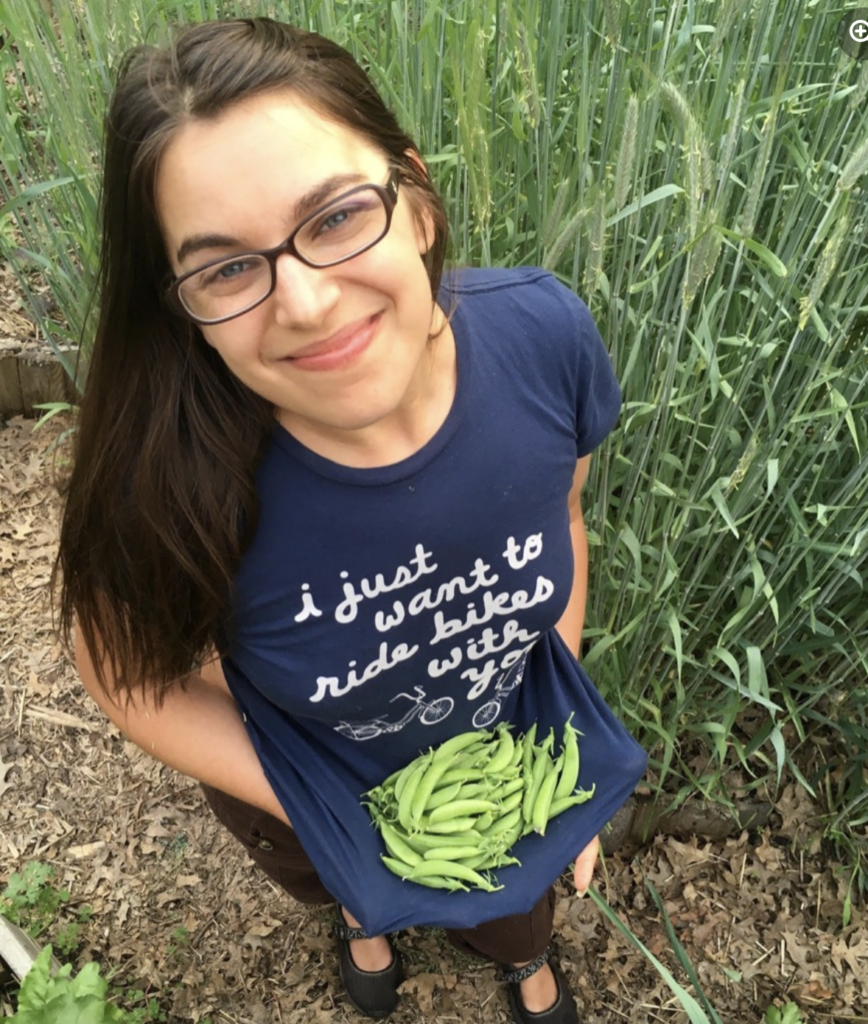 A young woman looking up and smiling while holding beans gathered in her tee-shirt being used as a "pouch". 